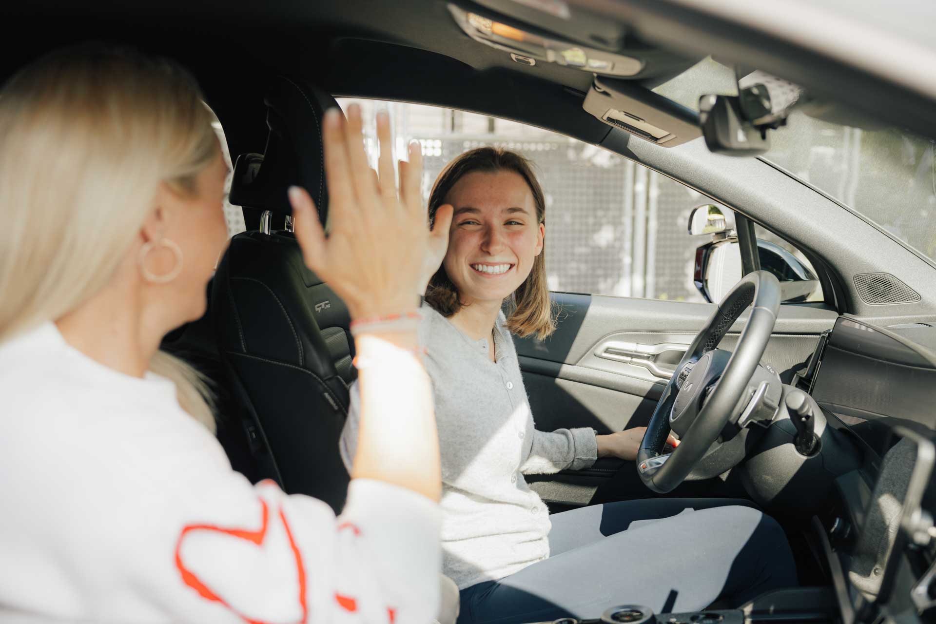Martina von der fahrschule kmh im Auto beim Unterricht, gibt High Five mit Schülerin.